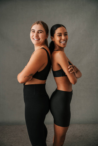 Девушки, стоящие там спортивная одежда спина к спине очень счастливы в спортзале студии. Высокое качество фото - Фото, изображение