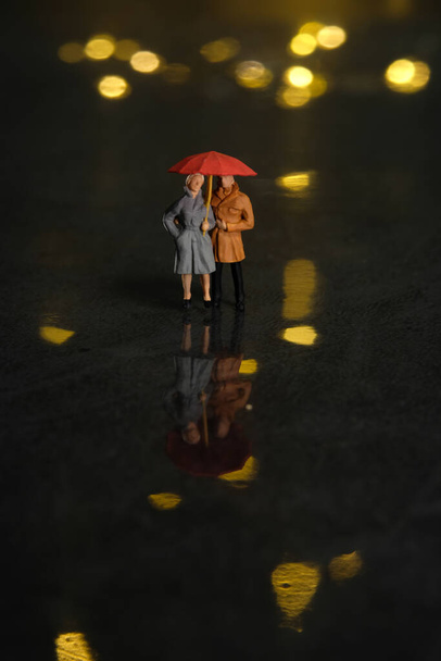 Personajes miniatura juguete figura fotografía. Pareja citas en día lluvioso usando paraguas en la noche. Hermoso amarillo dorado bokeh ciudad fondo claro. Foto de imagen - Foto, Imagen