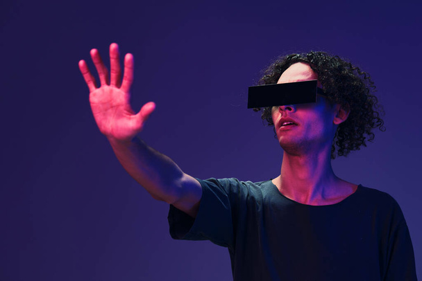 Innoissaan tyylikäs ruskettunut kihara mies musta t-paita silmälasit koskettaa näkymätön esine aiheuttaa eristetty väri vaaleanpunainen sininen tausta. Siisti muotitarjous. Virtual Reality uusi kokoelma käsite. Kopioi tila - Valokuva, kuva