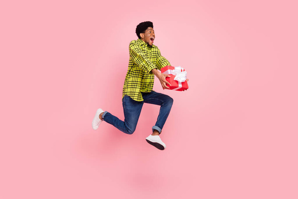 Full length photo of millennial sweet brunette guy jump hold present wear shirt jeans sneakers isolated on pink background. - Fotografie, Obrázek