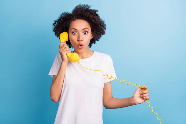 Portrait of attractive brunette amazed girl calling vintage yellow phone talking isolated over bright blue color background. - Photo, Image