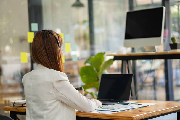 Sukces azjatyckiej bizneswoman siedzi przy biurku w słuchawkach rozmawiając z klientem online z laptopem. koncepcja rachunkowości finansowej - Zdjęcie, obraz