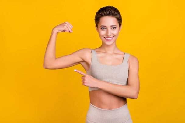 Photo of pretty strong lady direct finger strong biceps muscle wear grey top isolated yellow color background. - Foto, immagini