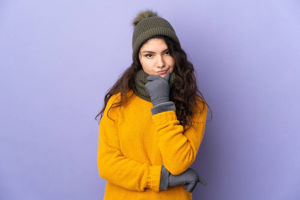 Teenager Russian girl with winter hat isolated on purple background thinking - Foto, imagen
