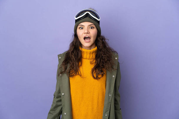 十代のロシアの女の子とともにスノーボードの眼鏡で紫色の背景に隔離されました驚きの顔の表情 - 写真・画像