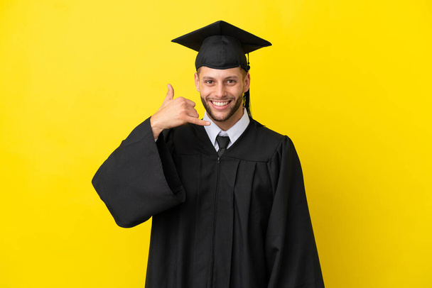 Молодой выпускник университета кавказский человек изолирован на жёлтом фоне, делая телефонный жест. Перезвони мне - Фото, изображение