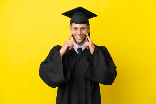 Молодой выпускник университета кавказский человек изолирован на желтом фоне улыбаясь со счастливым и приятным выражением - Фото, изображение