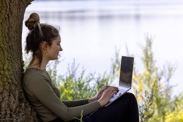 Arbeit von überall. Remote-Freelancer arbeiten in der Natur. Junge Frau, freie Mitarbeiterin, die mit Laptop arbeitet, mit wunderschönem Blick auf Wald und See. Freiberufler-Paradies, Freiheit der Telearbeit. Entfernung - Foto, Bild