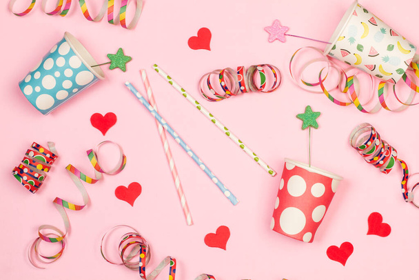 Papieren glazen, drinkrietjes, bloemenslingers en suikerrode hartjes op een roze achtergrond - Foto, afbeelding