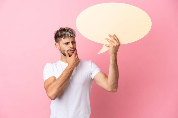 Young handsome caucasian man isolated on pink background holding an empty speech bubble and thinking - Foto, imagen
