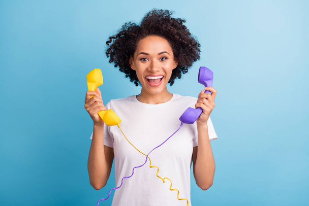 Portrait of young cheerful excited amazed african woman hold two cord telephones isolated on blue color background. - Fotografie, Obrázek