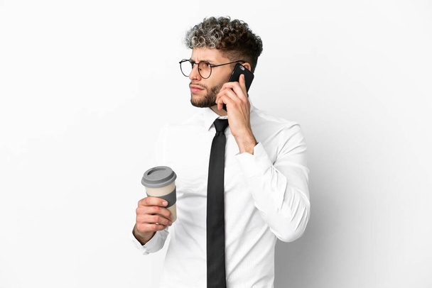 Business caucasian man isolated on white background holding coffee to take away and a mobile - Foto, Bild