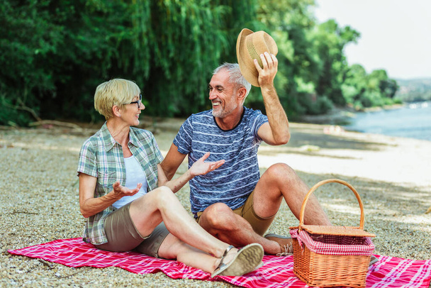 Linda pareja de ancianos disfrutando de tiempo de picnic en la orilla del río. - Foto, imagen