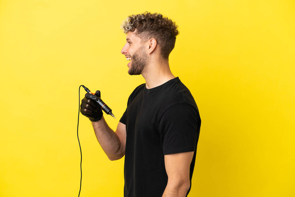 Tattoo artist caucasian man isolated on yellow background laughing in lateral position - Foto, immagini