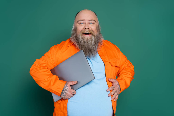 pleased overweight man with laptop touching tummy isolated on green - Foto, Imagem