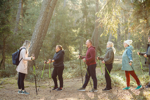 Coach femme blonde, entraîneur sportif avec un groupe de personnes enseignent scandinave, des exercices de marche nordique avec des bâtons dans la forêt, la nature. Mode de vie sain. Exercices de formation à la randonnée pour les équipes.  - Photo, image
