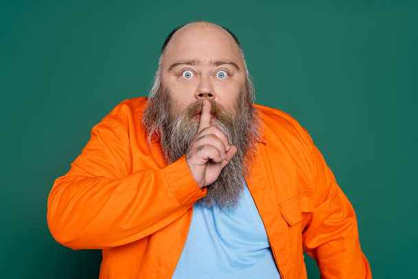 excited bearded man bulging eyes and showing hush sign isolated on green - Foto, afbeelding