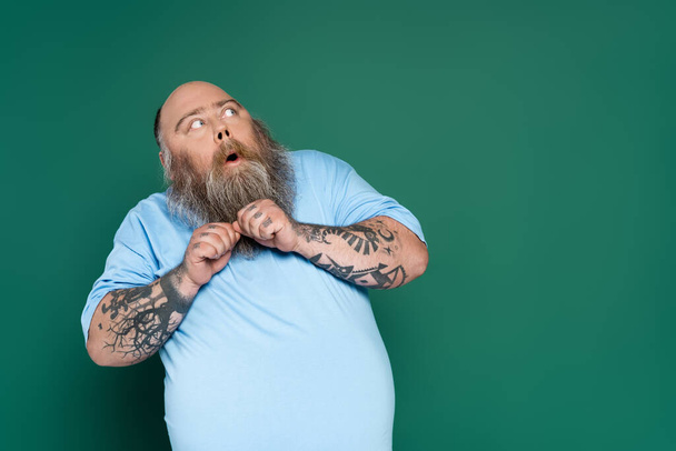 испуганный толстяк с бородой, смотрящий в сторону, изолированный на зеленый - Фото, изображение