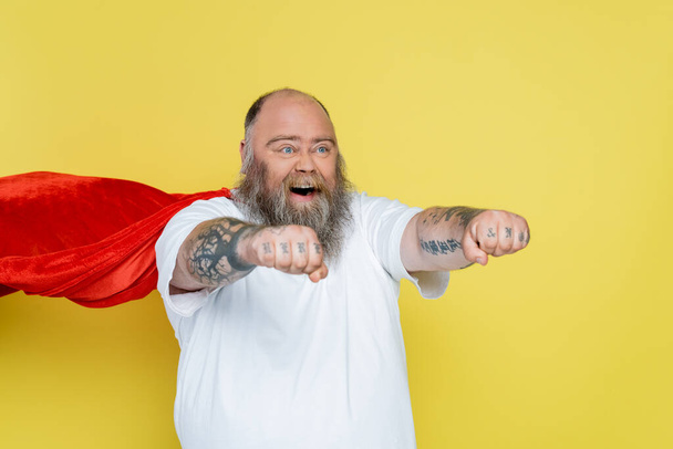 бородатий надмірна вага людини в костюмі супергероя, що кричить з витягнутими руками ізольовані на жовтому
 - Фото, зображення