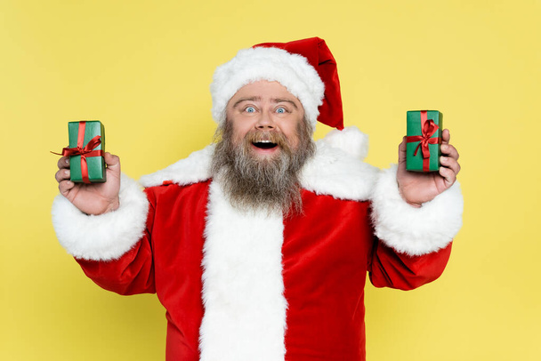 amazed overweight santa claus holding presents isolated on yellow - Foto, immagini