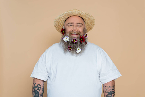 overweight man with decorated beard and straw hat smiling at camera isolated on beige - Foto, afbeelding