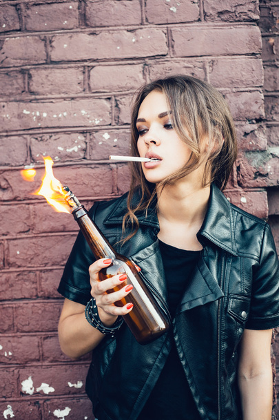 Bad young woman lighting up a cigarette from Molotov cocktail bomb in her hand - Foto, Imagen