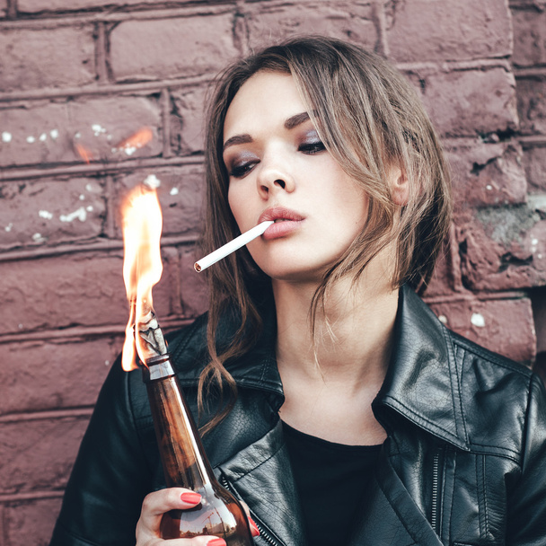 Woman hooligan lighting up a cigarette from Molotov cocktail bomb in her hand - 写真・画像