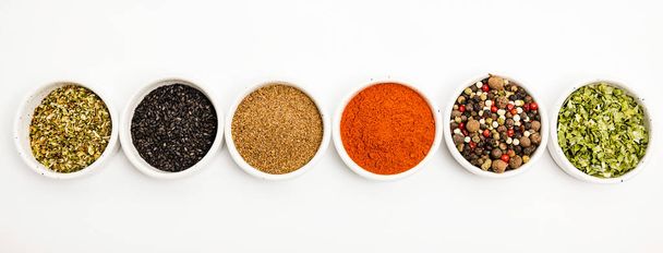 Types d'épices de différentes couleurs dispersées dans des bols en céramique isolés sur fond blanc. - Photo, image