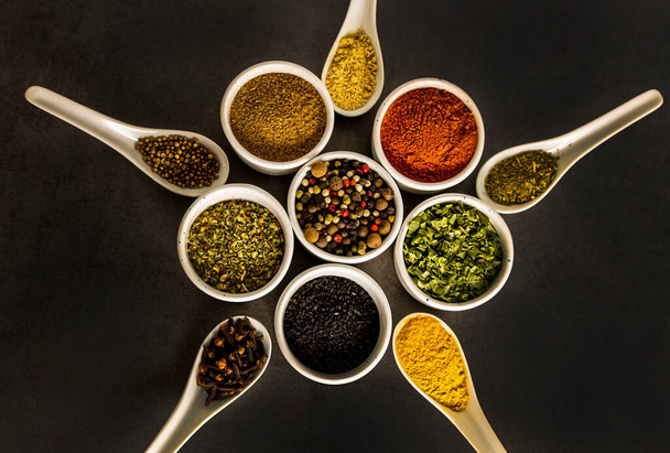 Spices of different varieties, laid out in the shape of a star, in white bowls and spoons, on a gray background, top view - 写真・画像