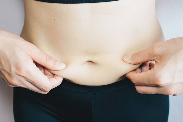Oříznutý záběr ženy dotýká její celulitidy tlusté břicho, žena ruka drží nadměrné břišní tuk. - Fotografie, Obrázek