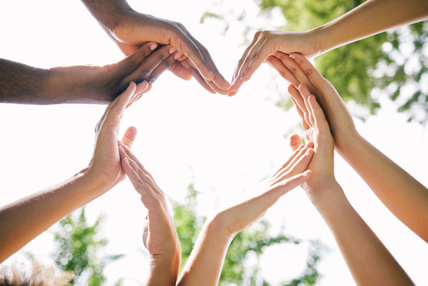 Multi-etnische handen maken een hart vorm buiten in de natuur. Closeup van een groep mensen die een hart maken als een concept van saamhorigheid en liefde. Multiculturele jongeren slaan handen ineen. - Foto, afbeelding