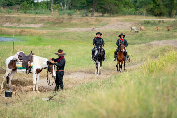 Два ковбоя на лошадях едут в деревню после окончания ухаживать за коровами на заднем плане. - Фото, изображение