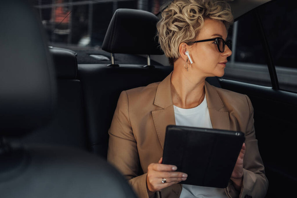 Žena podnikatelka dívá přes okno, zatímco sedí na zadní sedadlo luxusního auta - Fotografie, Obrázek