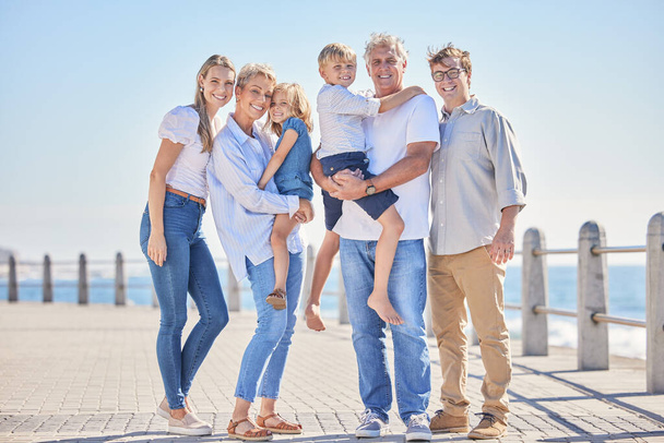 Full length portrait of happy caucasian multi-generation family standing together at the beach on a sunny day. Two little children enjoying time at the beach with their parents and grandparents. - 写真・画像