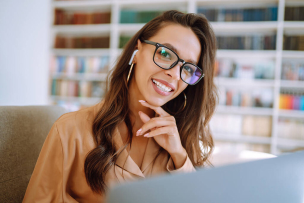 Young woman with wireless headphones calling on laptop, talk by webcam, video conference sitting on modern cafe. Freelancer working on a laptop. Business, online, education concept. - Foto, imagen