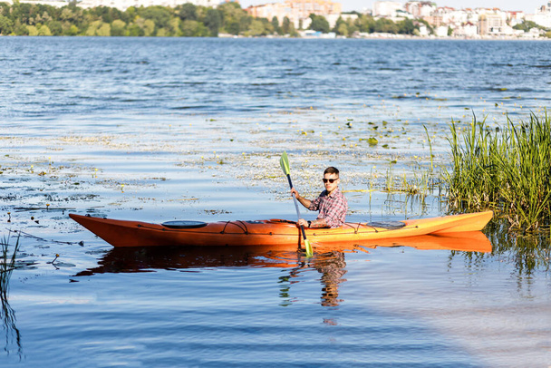 Kayaking on the river. A young Caucasian man sits in a kayak and paddles. The concept of water entertainment. - 写真・画像