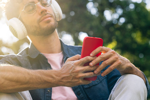 Portret przystojnego młodego hipstera słuchającego muzyki ze słuchawkami i telefonem komórkowym. - Zdjęcie, obraz