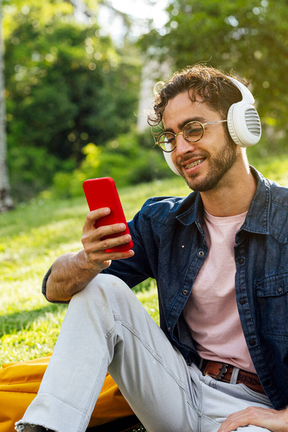Outdoor portrait of handsome young hipster man listening to music with headphones and mobile phone. - Φωτογραφία, εικόνα