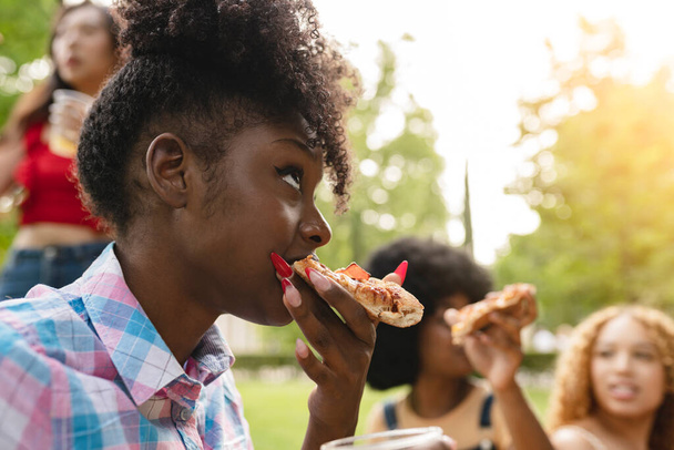 friends eat pizza in the park, focus african woman eating - Foto, Imagem