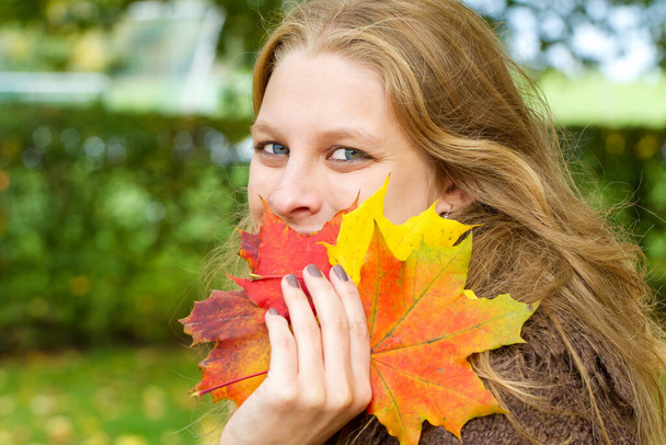 Νεαρή γυναίκα με πολύχρωμα φθινοπωρινά φύλλα στο χέρι - Φωτογραφία, εικόνα