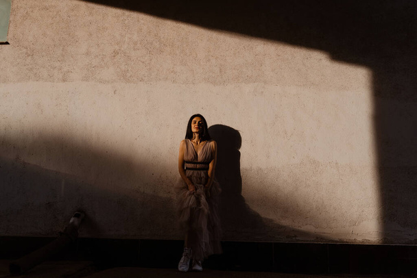 Gürcü tapılası kadın gün batımında sokakta gri duvar arkasında poz veriyor. Moda elbiseli çekici bir kız. - Fotoğraf, Görsel
