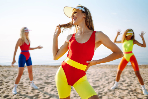Beautiful women in swimsuits are dancing on the beach. Three woman are training in the morning. Fitness, training, aerobics and people concept. Active sport. - Foto, immagini
