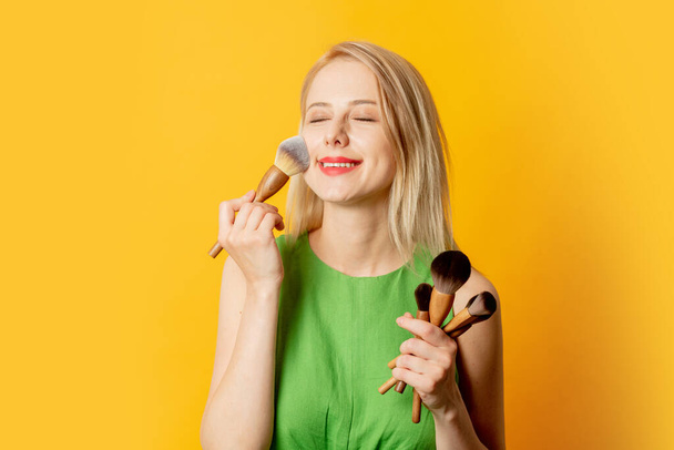 Stylish girl in green dress with makeup brushes on yellow background - Photo, Image