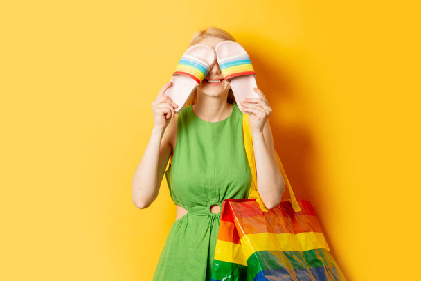 Chica con estilo con bolsa de arco iris y sandalias sobre fondo amarillo - Foto, Imagen
