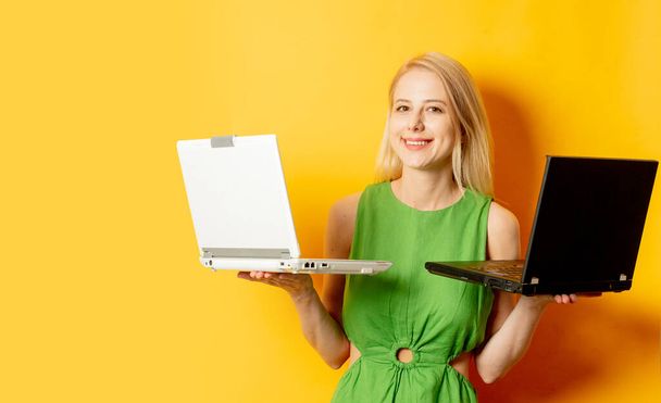 Stylish girl in green dress with two laptop computeres on yellow background - Фото, изображение