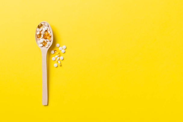 Vitamin capsules in a wooden spoon on a colored background. Pills served as a healthy meal. Drugs, pharmacy, medicine or medical healthycare concept. - Foto, Bild