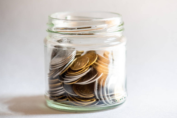 Heldere glazen pot voor tips met munten geld geïsoleerd op wit. Financieel concept - Foto, afbeelding