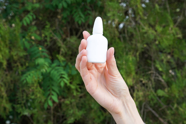Health and medical concept. Hand of a young woman holdin nasal drops outdoors.  - Photo, Image