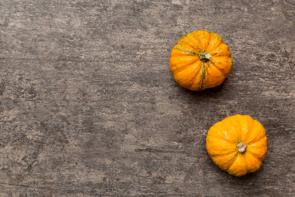 着色されたテーブルの背景に小さなオレンジ色のカボチャの秋の組成。秋、ハロウィンと感謝祭のコンセプト。秋のフラットレイアウト写真。コピースペースでのトップビュー. - 写真・画像