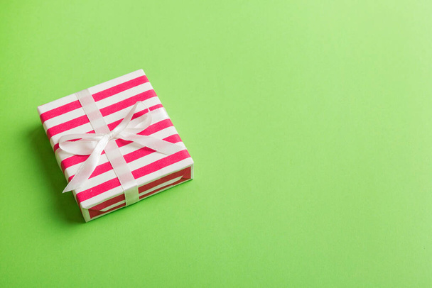 verpakt Kerstmis of andere vakantie handgemaakte geschenkdoos in kleur papier met lint op gekleurde achtergrond. Aanwezig doos, decoratie van geschenk op gekleurde tafel, bovenaanzicht met kopieerruimte. - Foto, afbeelding